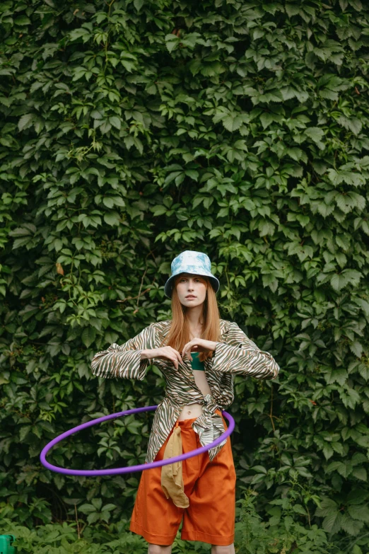 a woman standing in front of a bush with a hula hoop, trending on pexels, magic realism, sadie sink, with hat, sandro botticelli style, tribal clothing