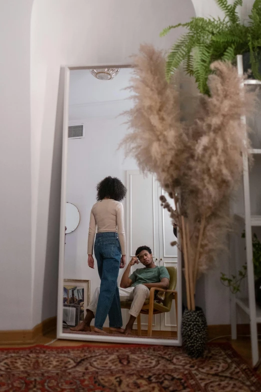 a woman standing in front of a mirror next to a man, a picture, trending on pexels, tall plants, in a comfortable chair, people looking at a house, afro hair