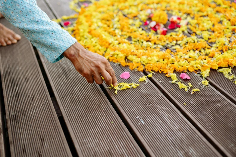 a close up of a person touching a flower on a wooden floor, a mosaic, ceremonial ritual, teak table, with yellow flowers around it, blossoming path to heaven