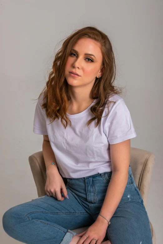 a beautiful young woman sitting on top of a chair, trending on pexels, photorealism, plain white tshirt, coiffed brown hair, pr shoot, jeans and t shirt