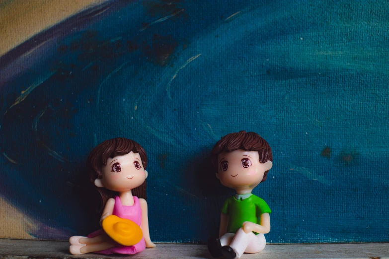 a couple of figurines sitting next to each other, a picture, by Julia Pishtar, pexels contest winner, children's animated films, background image, blue and green colours, sitting on the floor