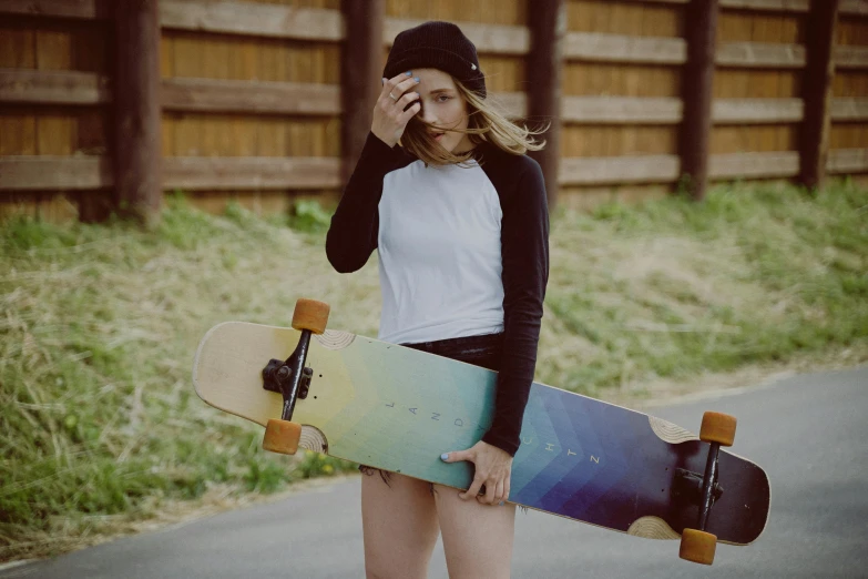 a woman standing on the side of a road holding a skateboard, a picture, by Julia Pishtar, iridescent visor, sport bra and dark blue shorts, federation clothing, thumbnail