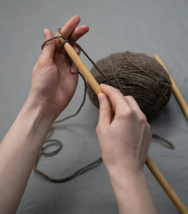 a close up of a person knitting a ball of yarn, by Matthias Stom, unsplash, wearing a brown, she is holding a long staff, on a gray background, repeating