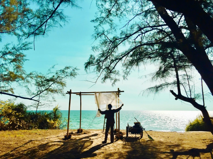 a man standing on top of a sandy beach next to the ocean, in style of thawan duchanee, campsites, profile image