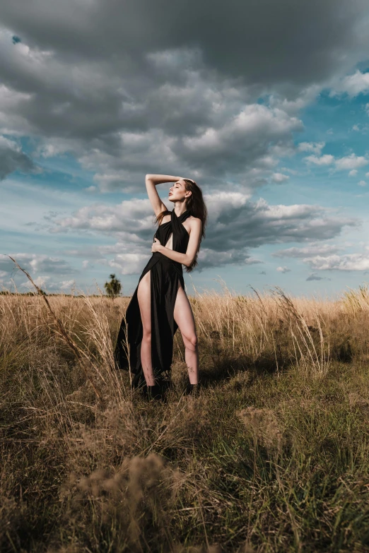 a woman in a black dress standing in a field, an album cover, unsplash, fashion model pose, 2019 trending photo, wide angle full body, modeled