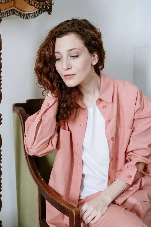 a woman sitting in a chair next to a lamp, a portrait, inspired by Anita Malfatti, trending on pexels, renaissance, cropped shirt with jacket, coral brown hair, curly pink hair, wearing a linen shirt