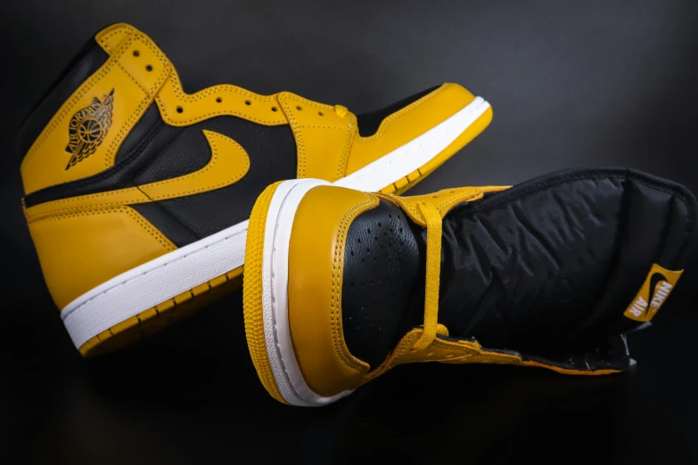 a pair of yellow and black sneakers on a black surface, trending on unsplash, hyperrealism, air jordan 1 high, colors: yellow, leather padding, detailed shot legs-up