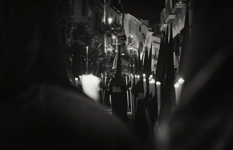 a couple of people walking down a street at night, a black and white photo, by Giuseppe Avanzi, unsplash, renaissance, white candles, parade, traditional corsican, distant hooded figures