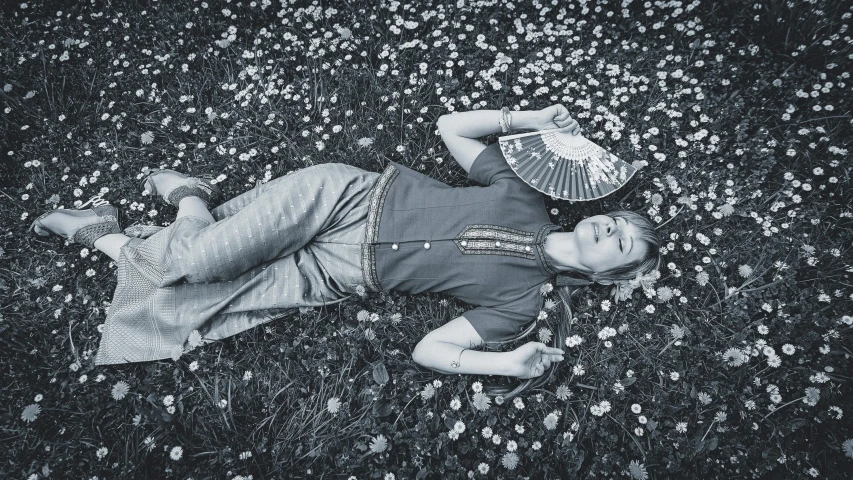 a black and white photo of a woman laying in a field of daisies, inspired by Grete Stern, magic realism, in a blue qipao, maisie williams, resting after a hard fight, sha xi