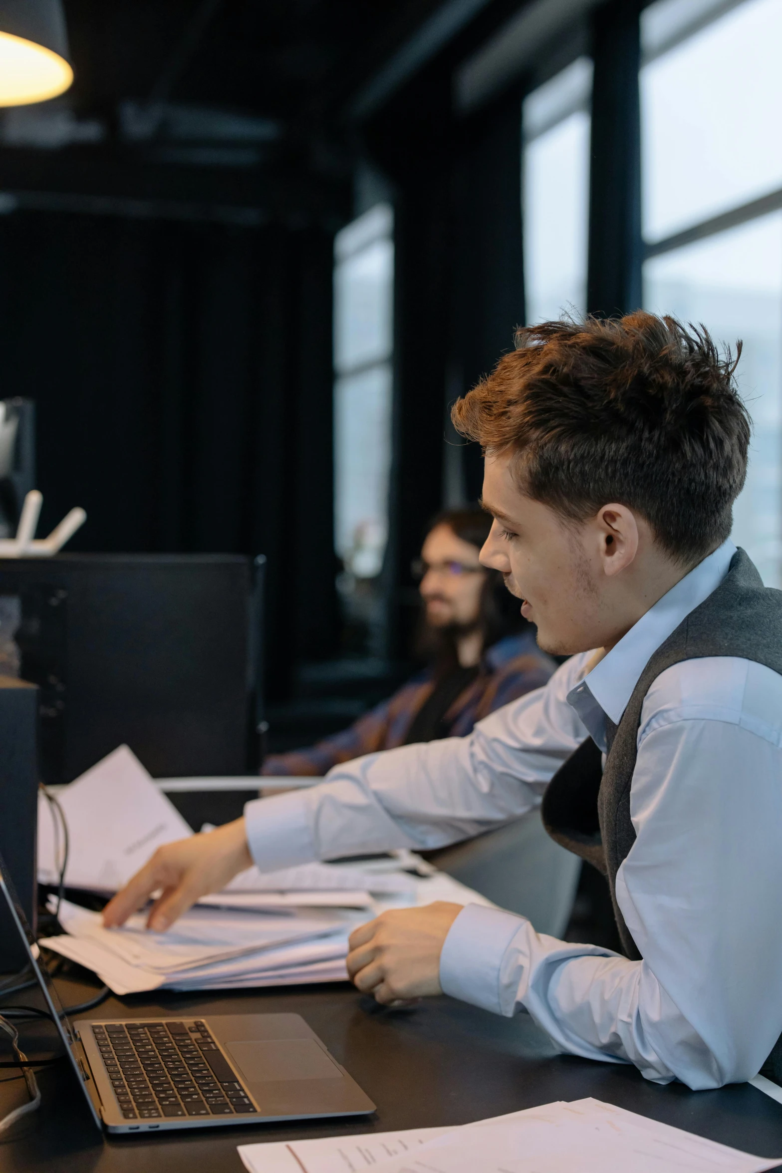 a man sitting at a desk working on a laptop, by Jacob Toorenvliet, reddit, dynamic scene, production photo, magnus carlsen, lachlan bailey