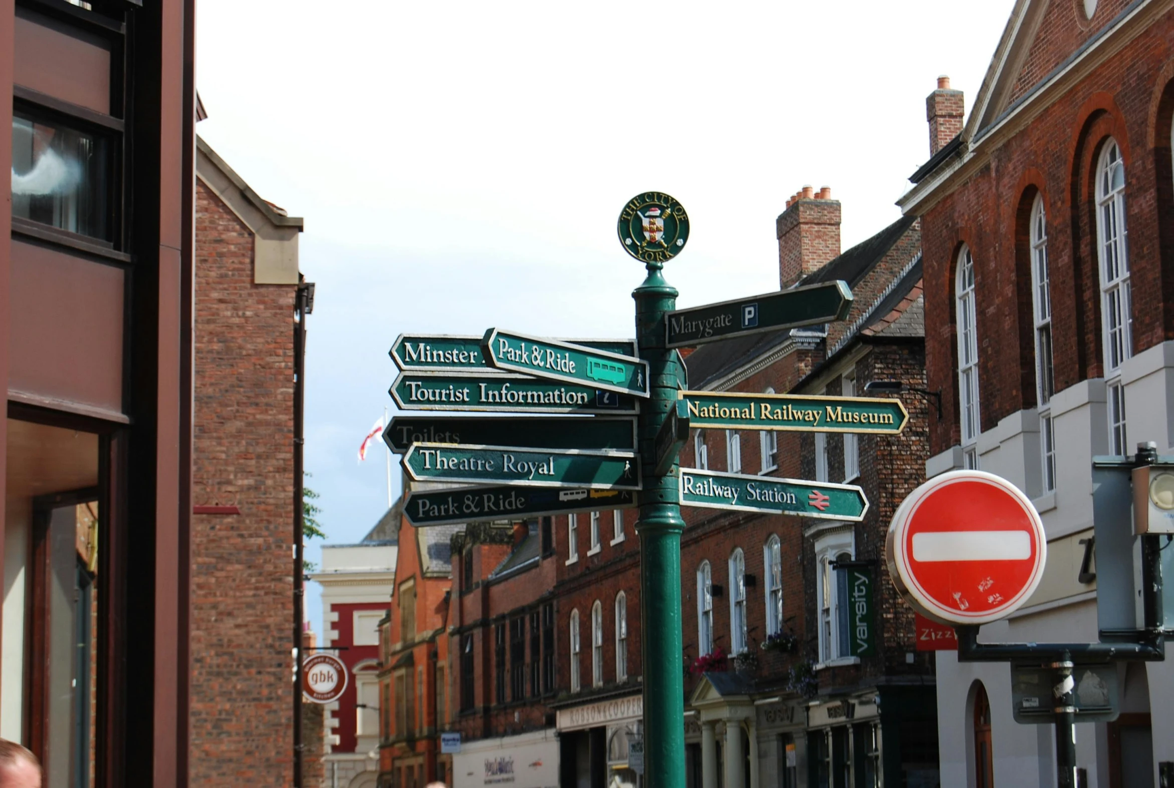 a green street sign sitting on the side of a road, by David Simpson, unsplash, arts and crafts movement, red bricks, lots of signs and shops, 2 2 nd century!!!!! town street, preserved historical