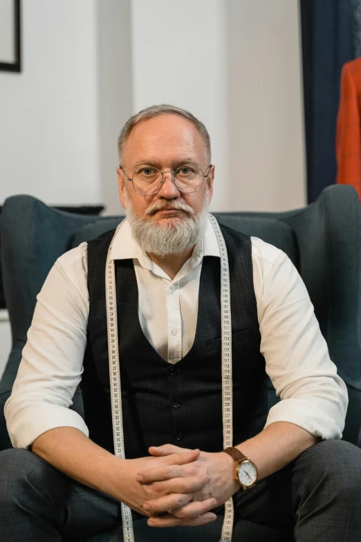 a man sitting in a chair with a measuring tape around his waist, by János Nagy Balogh, trending on reddit, wearing a vest and a tie, silver full beard, professional profile photo, andrzej duda