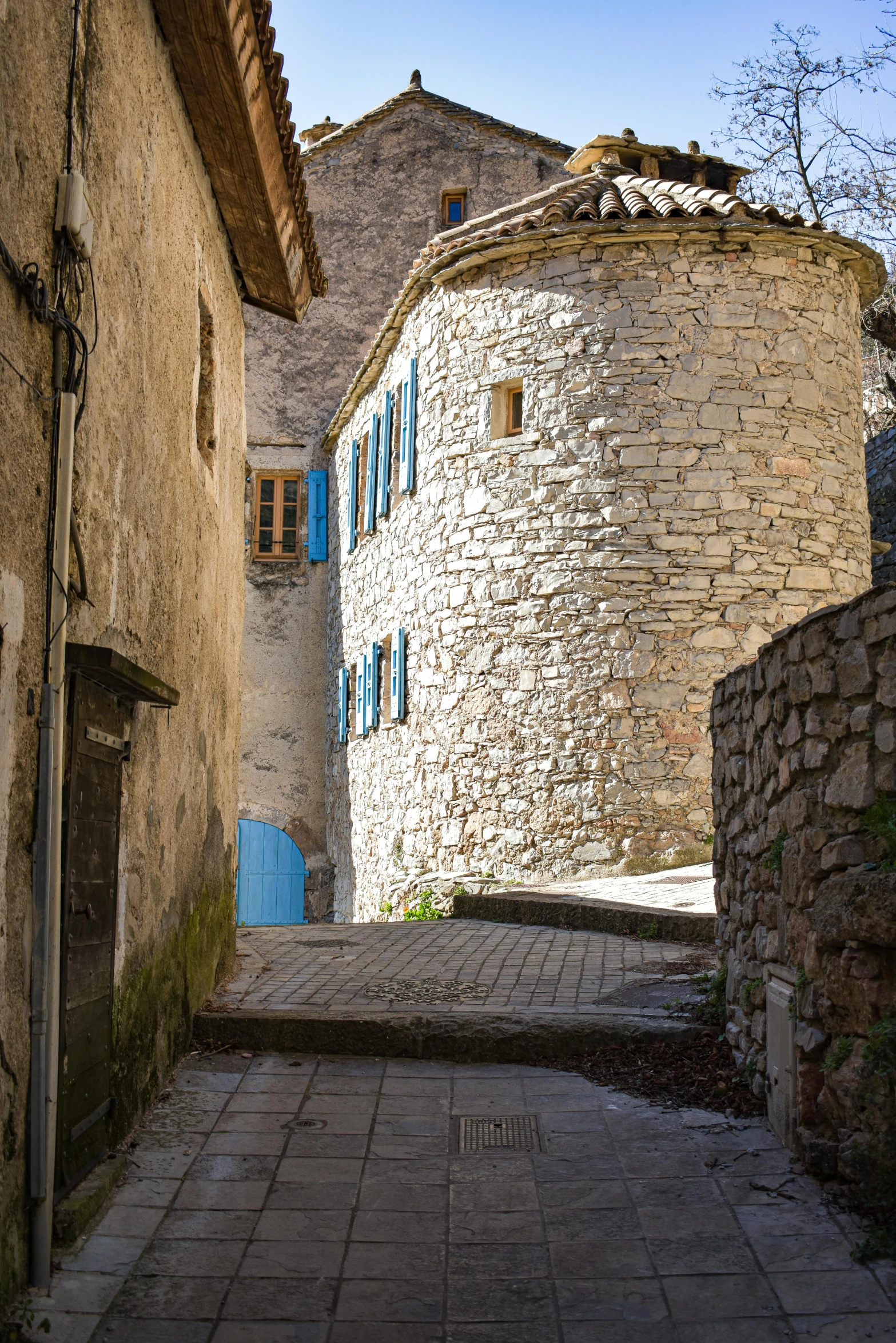 a narrow alley with a stone building in the background, inspired by Pierre Toutain-Dorbec, romanesque, rounded architecture, cyan shutters on windows, cliffside town, photographs