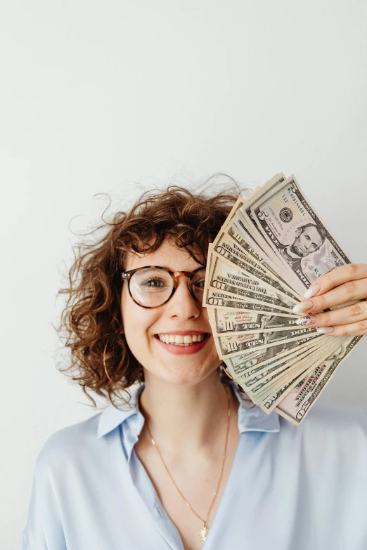 a woman holding a fan of money in front of her face, pexels contest winner, wearing medium - sized glasses, wavy hair spread out, a still of a happy, a person standing in front of a