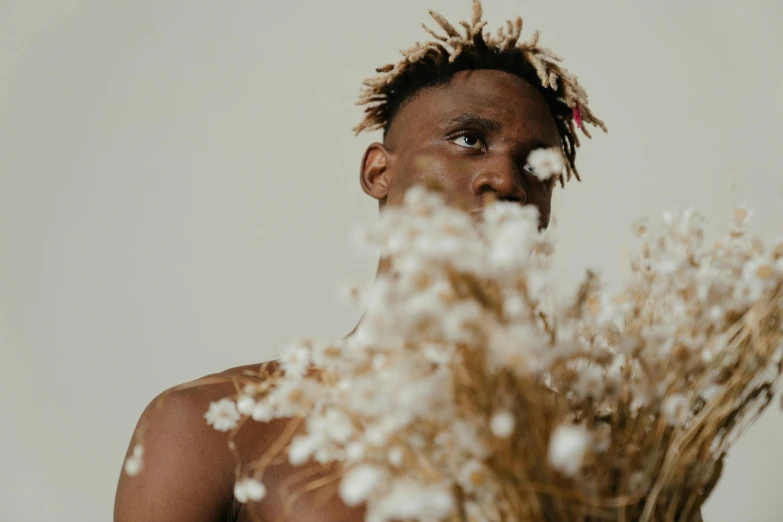 a man with dreadlocks holding a bunch of flowers, by Matija Jama, trending on pexels, afrofuturism, brown and white color scheme, bare shoulders, photoshoot for skincare brand, gold flowers