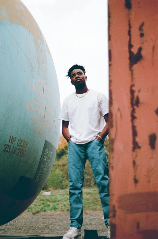 a man standing next to a large metal object, by Stokely Webster, 2 1 savage, high quality upload, slightly smiling, silo