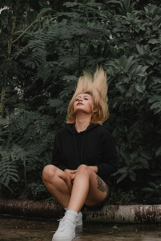 a woman sitting on the ground with her hair in the air, an album cover, inspired by Elsa Bleda, pexels contest winner, realism, lush greenery, black hoodie, short curly blonde haired girl, unsplash transparent