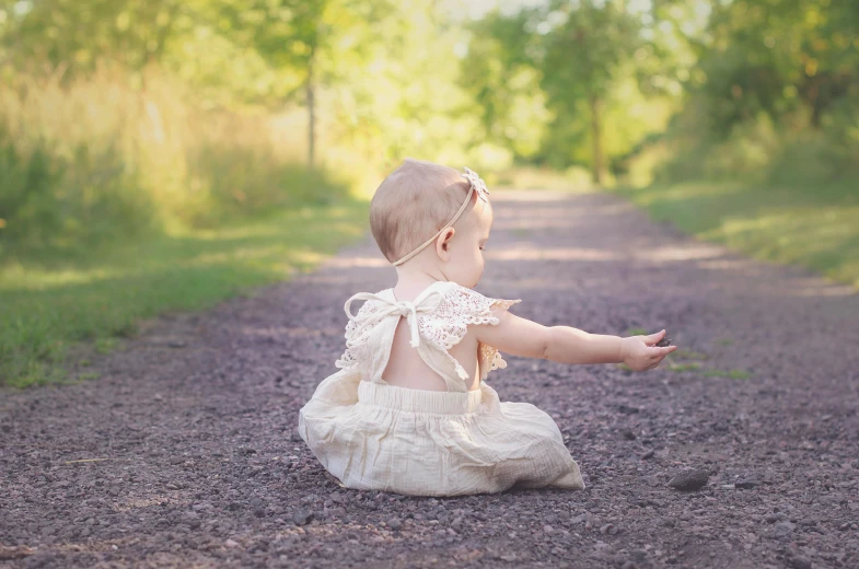 a baby sitting in the middle of a dirt road, elegant posed, lane brown, aurora aksnes, handcrafted