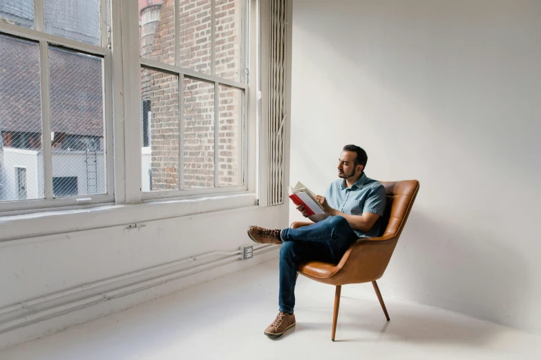 a man sitting in a chair reading a book, by Will Ellis, light and space, window, riyahd cassiem, profile image, sitting on designer chair