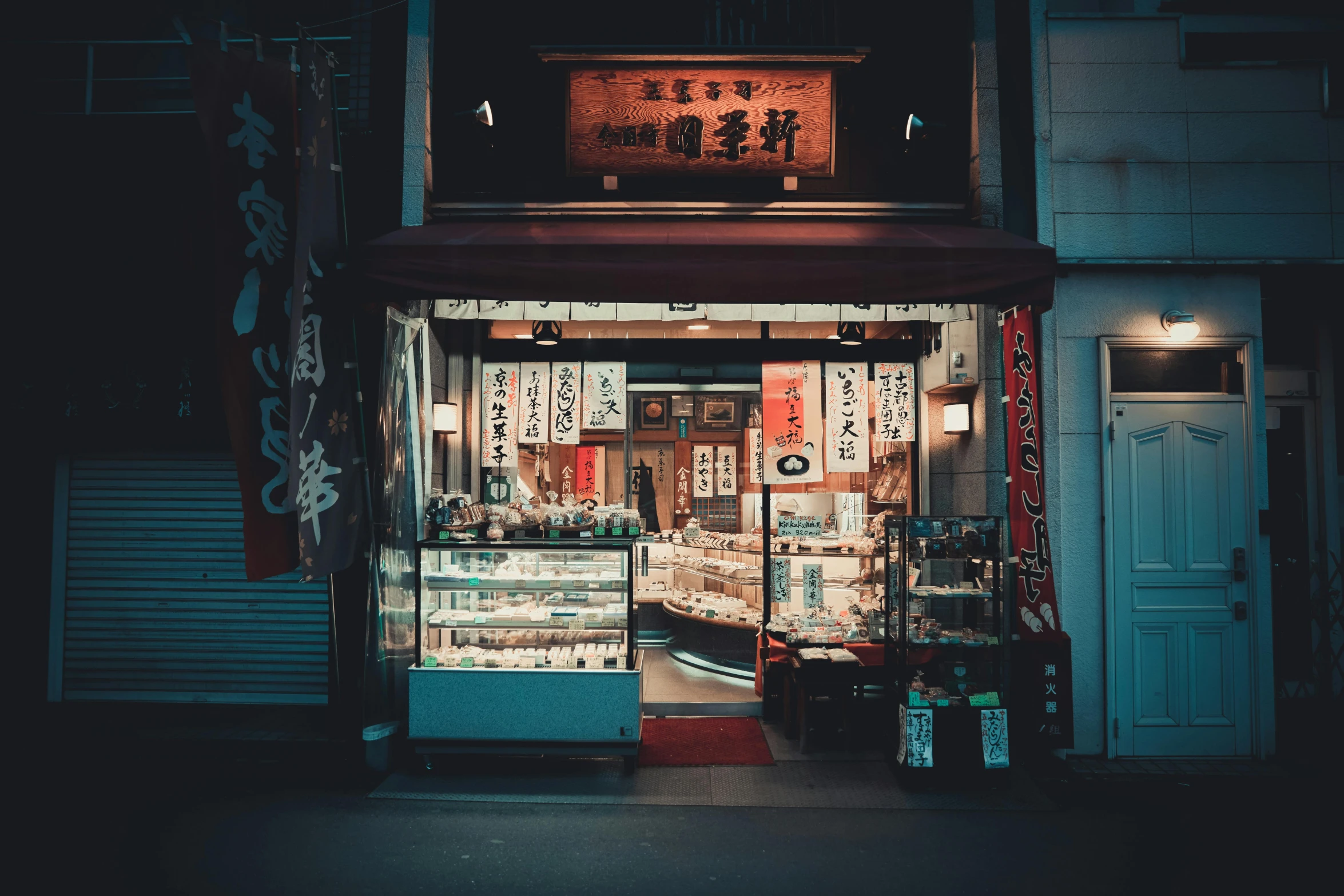 a store front on a city street at night, inspired by Kanō Naizen, unsplash contest winner, ethnicity : japanese, sweets, vintage photo, small buildings