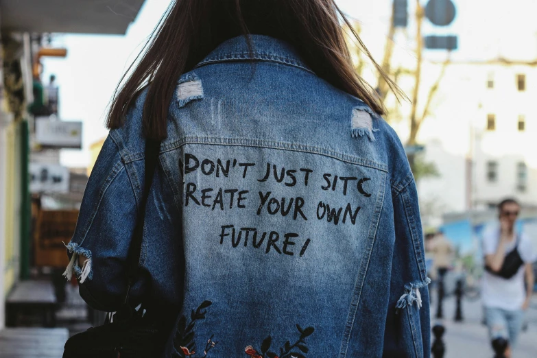 a woman wearing a denim jacket with writing on it, a picture, by Julia Pishtar, trending on pexels, cyber future jacket, diy, schools, still photograph