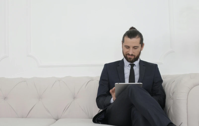 a man in a suit sitting on a couch using a tablet, inspired by Sava Šumanović, pexels, arbeitsrat für kunst, mid long hair, caucasian, 2 4 years old, slightly minimal