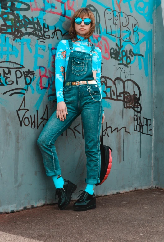 a woman leaning against a wall with graffiti on it, an album cover, inspired by Elsa Bleda, trending on pexels, blue overalls, full body!! maximalist details, better known as amouranth, trending on r/streetwear