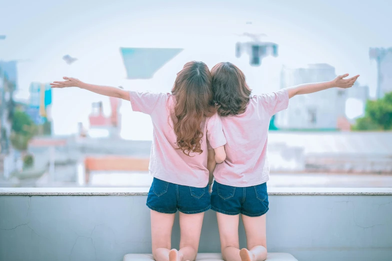 a couple of little girls standing next to each other, pexels contest winner, wearing shorts and t shirt, from back, the sky is pink, asian women