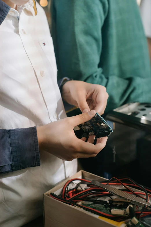 a couple of people standing next to each other, trending on pexels, happening, smoking soldering iron, holds a smart phone in one hand, environmental shot, computer components