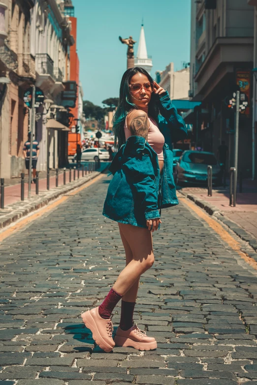 a woman standing on a cobblestone street talking on a cell phone, an album cover, by Alejandro Obregón, pexels contest winner, hyperrealism, bra and shorts streetwear, teal skin, jacket, of taiwanese girl with tattoos
