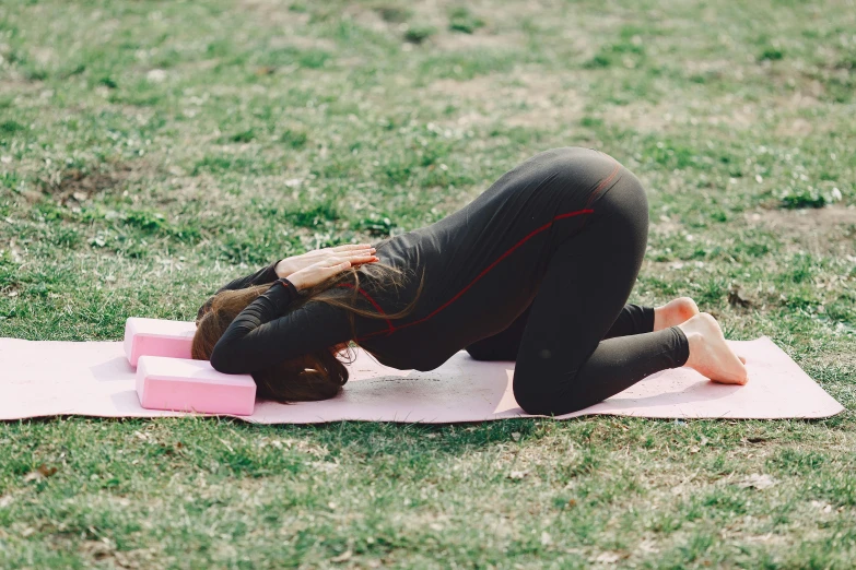 a woman doing a yoga pose on a pink mat, by Rachel Reckitt, unsplash, hurufiyya, in a park, lower back, sleepy, brown