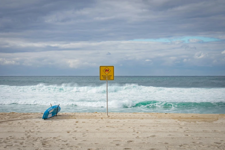 a yellow sign sitting on top of a sandy beach, by Peter Churcher, unsplash contest winner, happening, massive waves, square, manly, zac retz