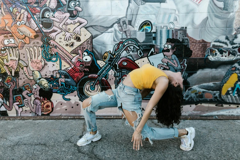 a woman doing a handstand in front of a graffiti wall, pexels contest winner, graffiti, wearing yellow croptop, background image, artist wearing torn overalls, sitting down