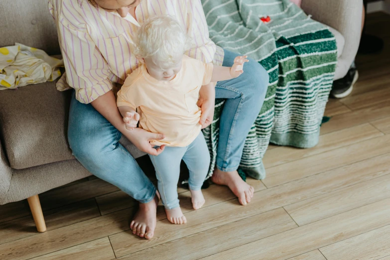 a woman sitting on a couch holding a baby, trending on pexels, pants, a wooden, background image, sitting on the floor