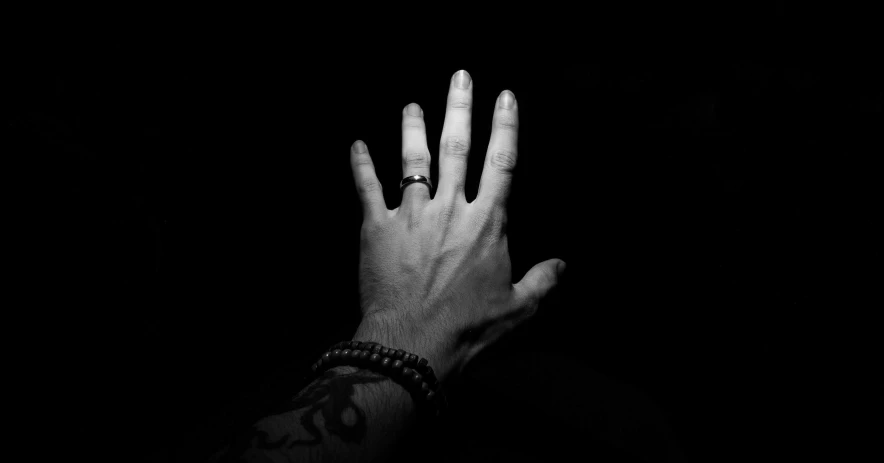 a person holding their hand up in the dark, a black and white photo, by Kristian Zahrtmann, pexels, wearing two metallic rings, black and white tattoo, album cover, no man