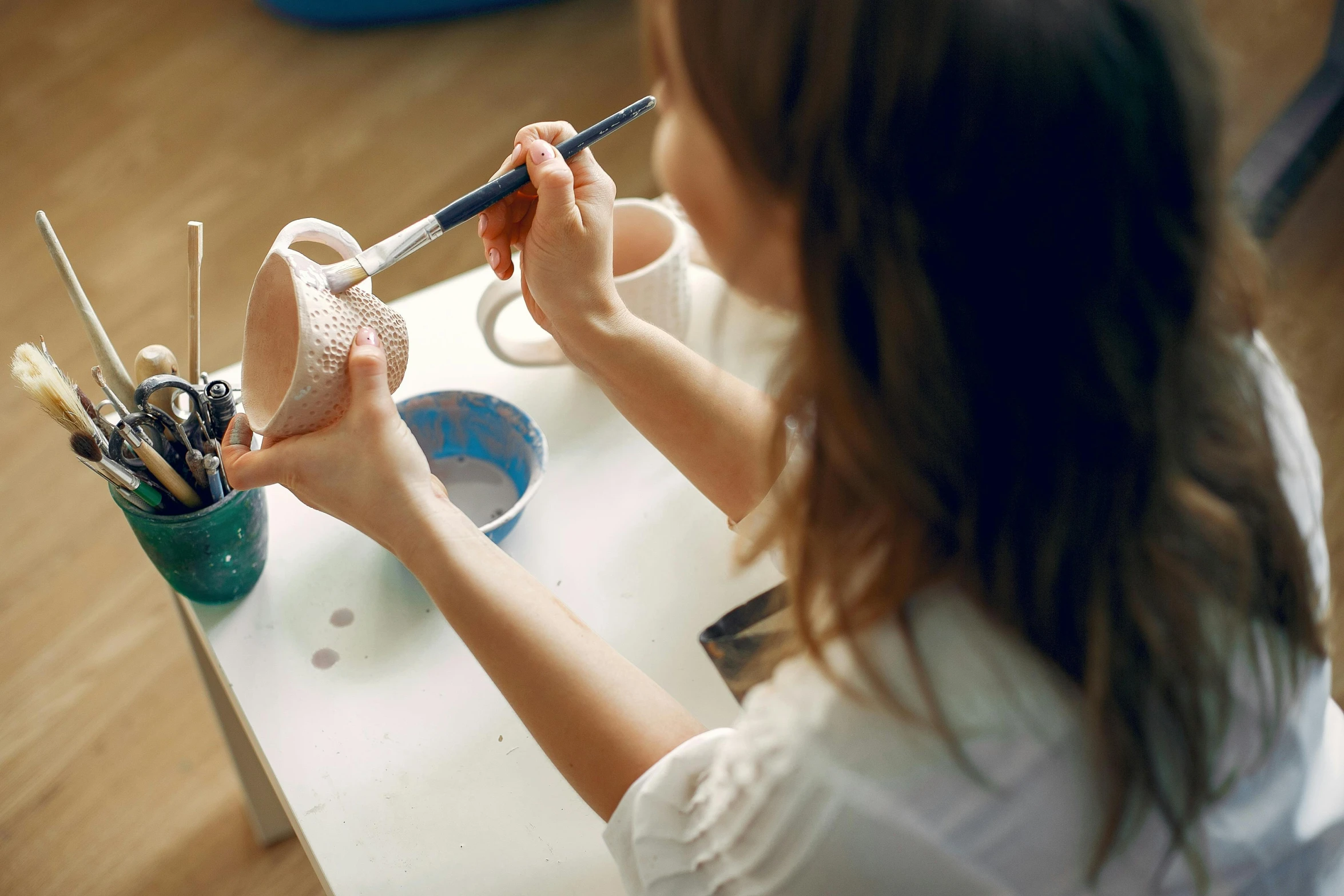 a woman sitting at a table with a brush in her hand, pexels contest winner, process art, white ceramic shapes, teenage girl, ready-made, finely textured