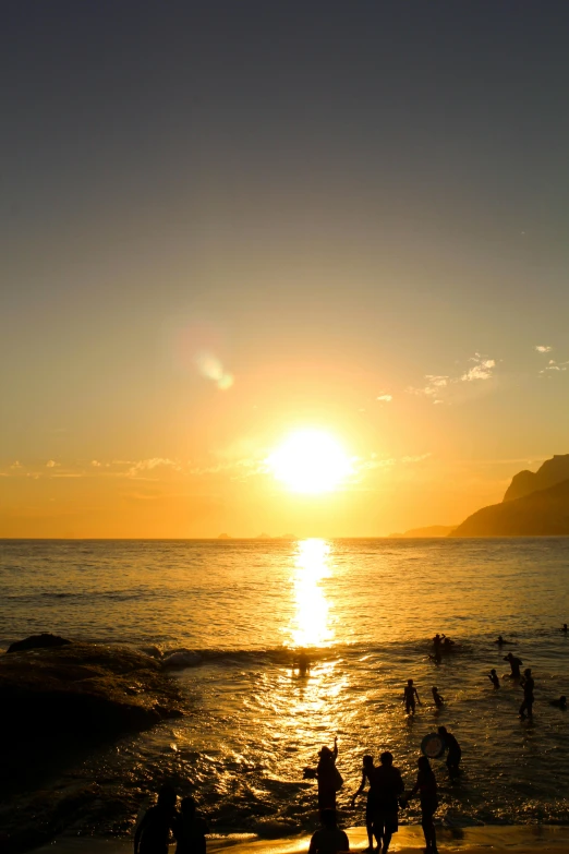 a group of people standing on top of a sandy beach, during a sunset, monaco, gigantic sun, ((sunset))