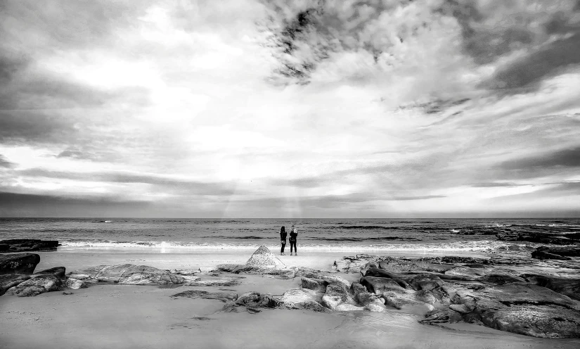 a couple of people standing on top of a sandy beach, a black and white photo, with backdrop of god rays, south african coast, listing image, liquid light