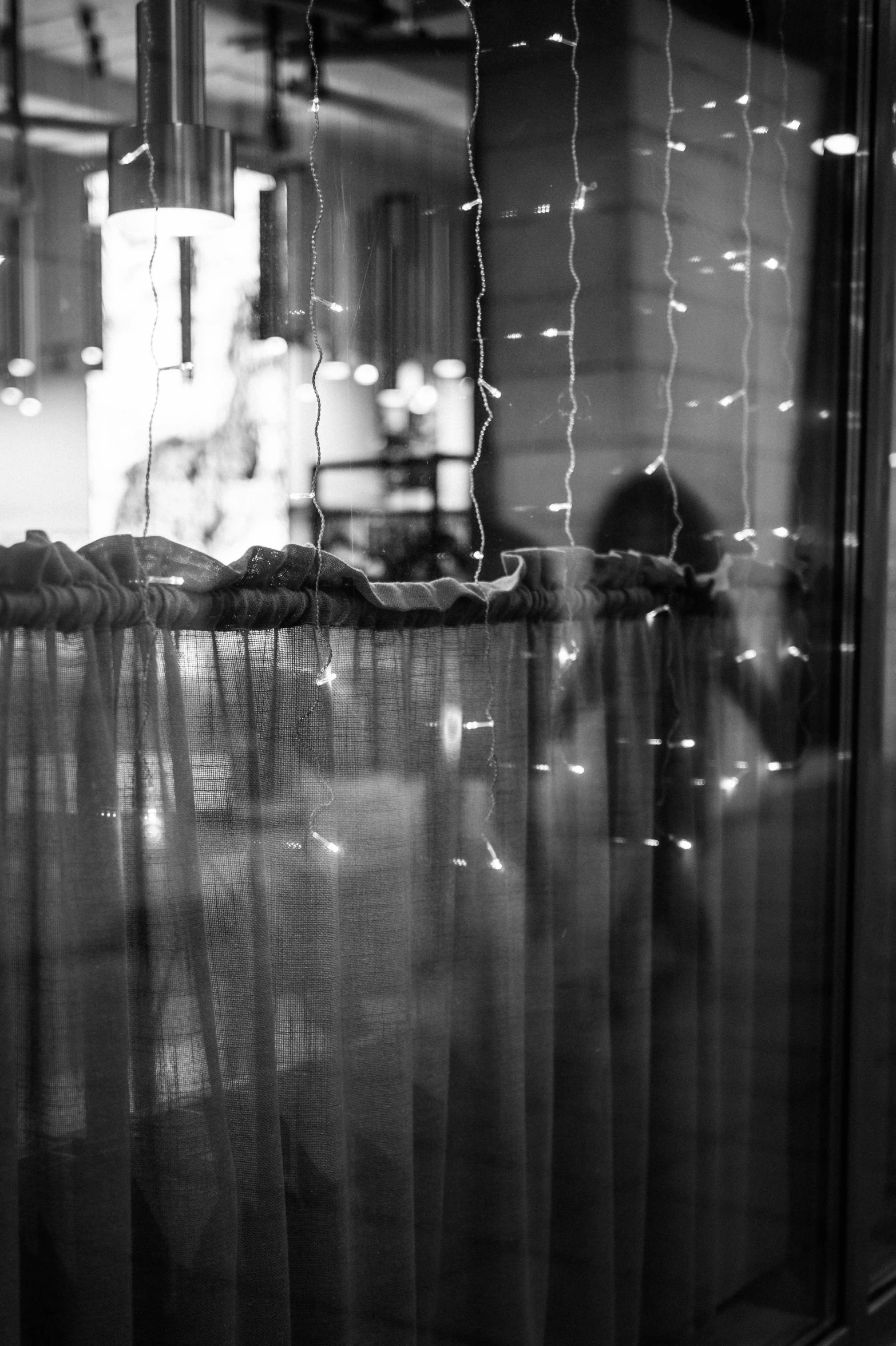 a pizza sitting on top of a table in front of a window, a black and white photo, inspired by Vivian Maier, unsplash, ethereal curtain, people at night, full of glass. cgsociety, glass and lights