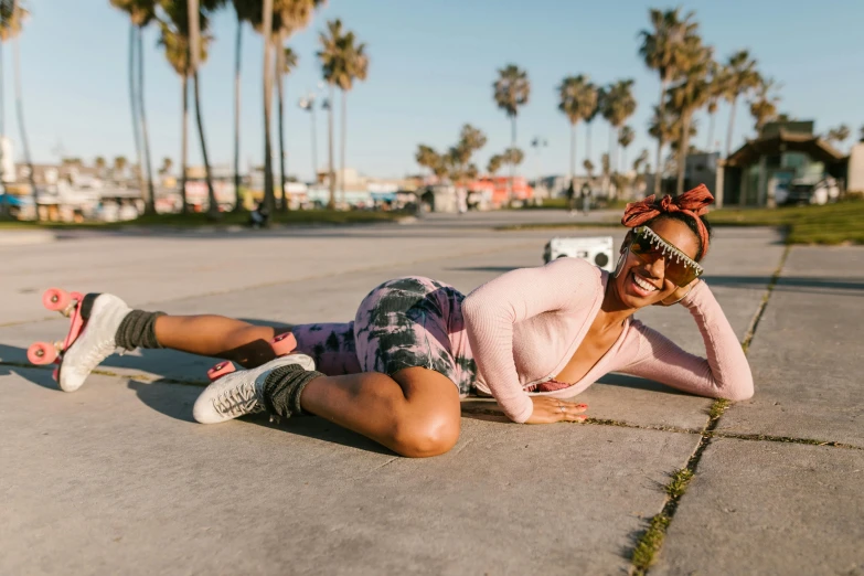 a woman laying on the ground with palm trees in the background, by Nina Hamnett, pexels contest winner, happening, rollerskaters, photo of a black woman, woman with rose tinted glasses, patterned clothing