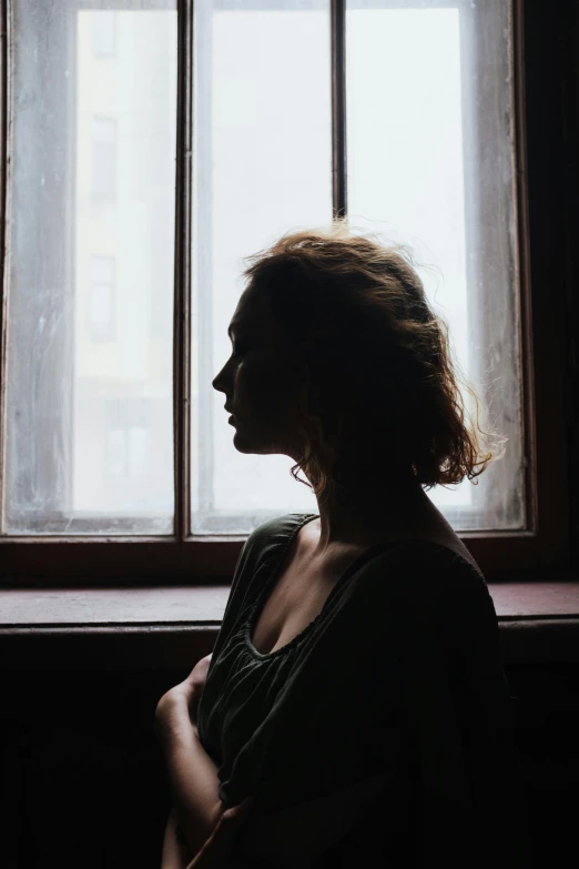 a woman sitting in front of a window, inspired by Elsa Bleda, pexels contest winner, renaissance, head turned to the side, silhouette of man, wistful bosom, depressed mood