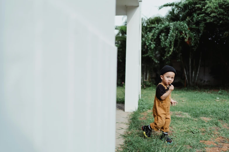 a little boy that is standing in the grass, by Basuki Abdullah, pexels contest winner, minimalism, jumpsuit, brown pants, outlive streetwear collection, katelynn mini cute style