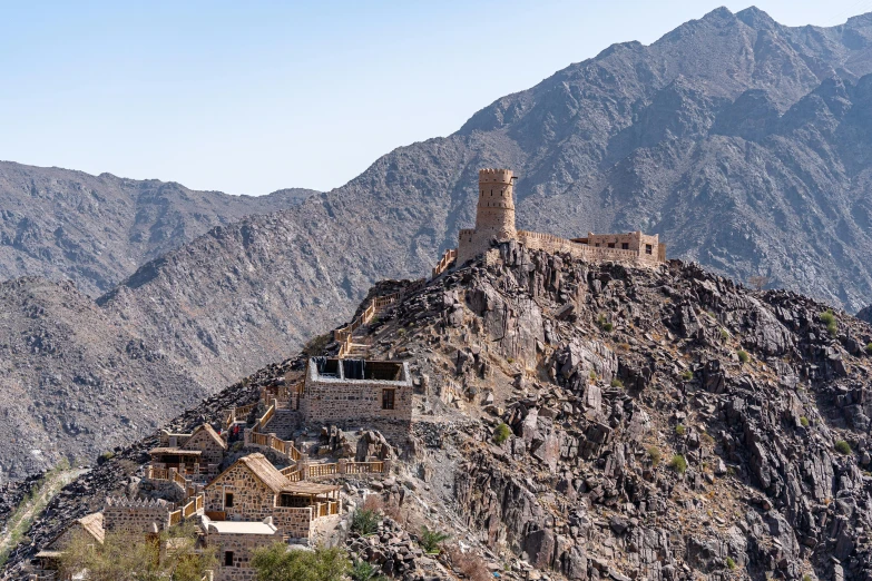 a castle on top of a mountain with mountains in the background, a photo, oman, brutalist buildings tower over, portrait image