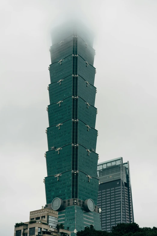 a very tall building in the middle of a city, inspired by Cheng Jiasui, under a gray foggy sky, square, taiwan, close-up!!!!!