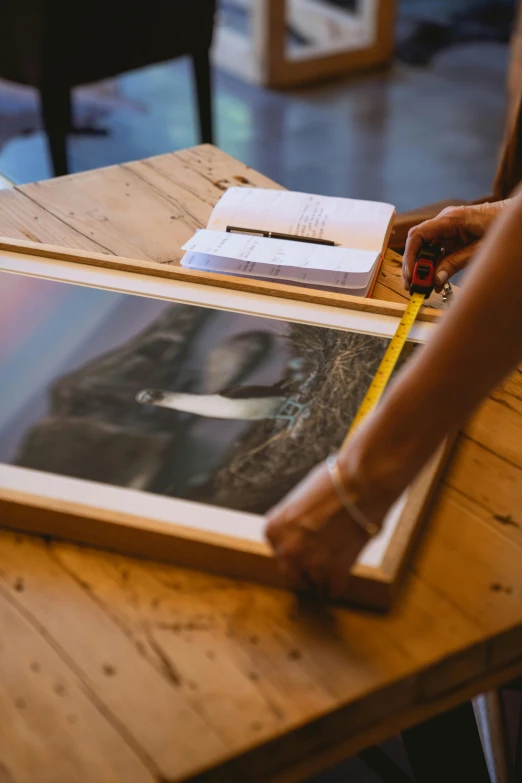 a person that is holding a picture on a table, poster art, taken at golden hour, inspect in inventory image, on a wooden tray, performing