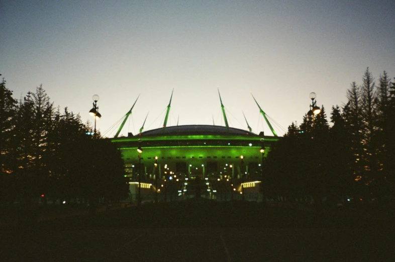 a green stadium lit up at night with trees in the foreground, an album cover, unsplash contest winner, brutalism, saint petersburg, dome, pale green glow, fujicolor with flash