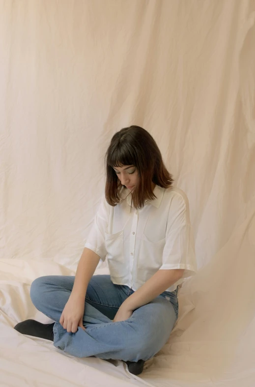 a woman sitting on top of a bed next to a cat, an album cover, by Louisa Chase, trending on unsplash, wearing a white button up shirt, center parted curtain bangs, studio shoot, meditation pose