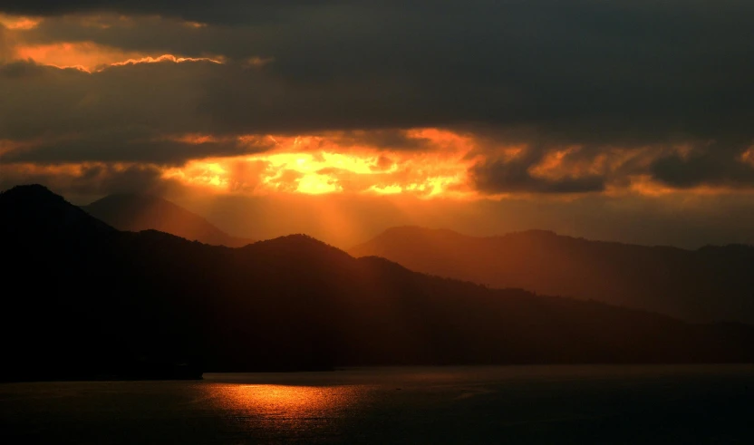 a large body of water with mountains in the background, pexels contest winner, sumatraism, sun shafts, dramatic lightin, shades of gold display naturally, god light