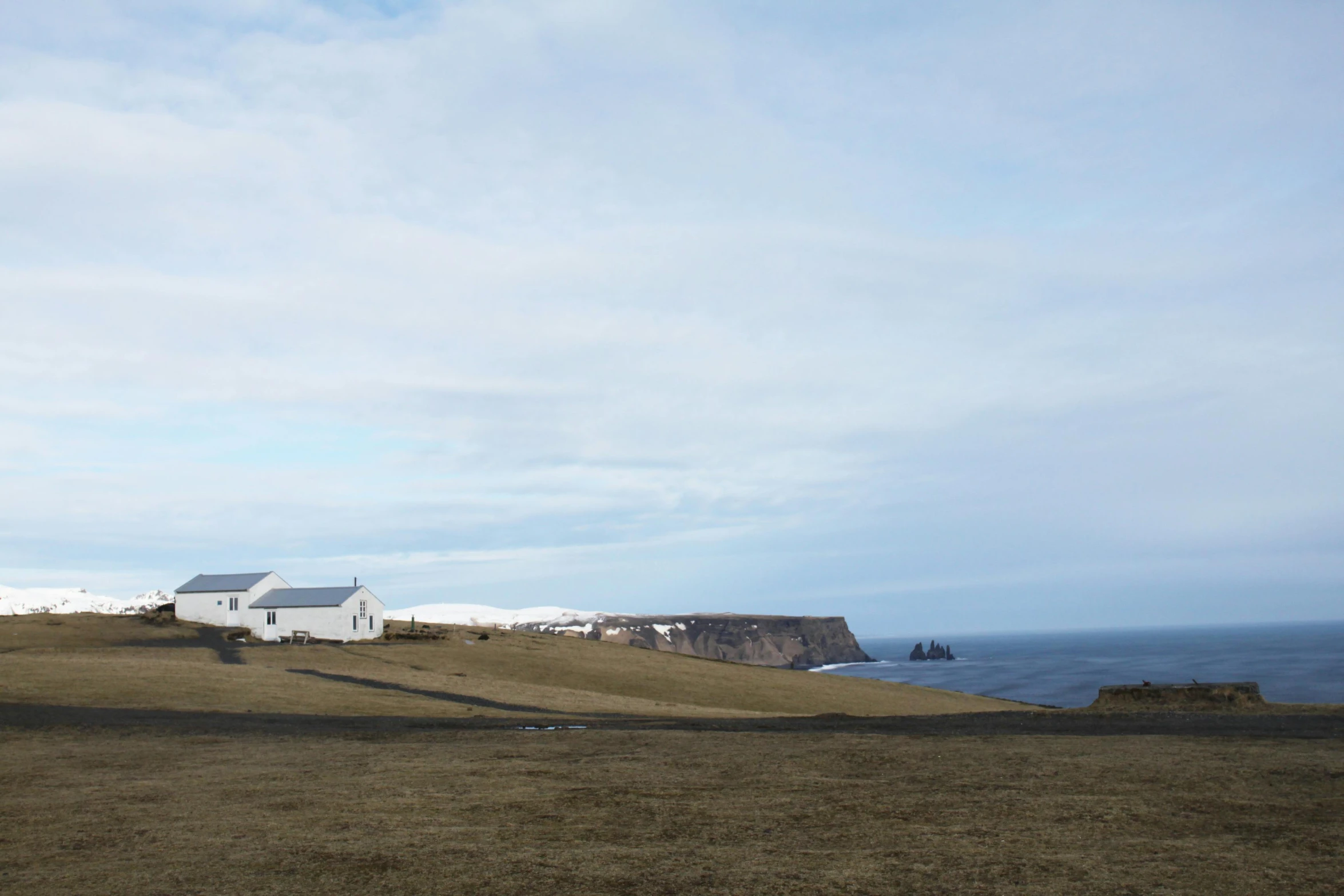 a man flying a kite on top of a grass covered field, by Hallsteinn Sigurðsson, happening, whitewashed buildings, views to the ocean, the photo was taken from afar, on an island