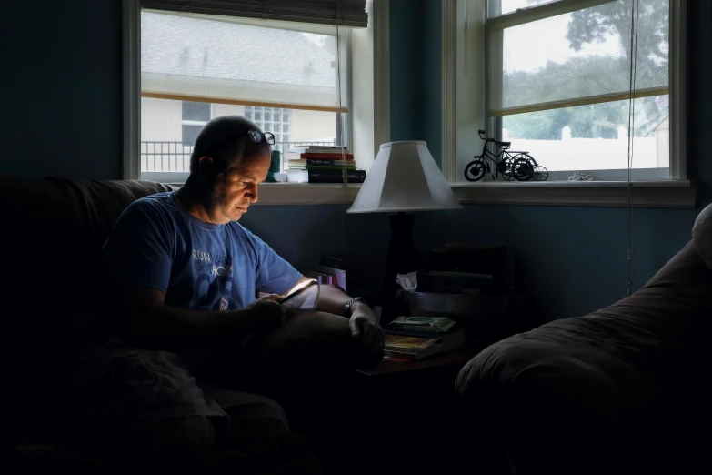 a man sitting on a couch reading a book, by Carey Morris, strong backlight, someone in home sits in bed, ap news, taken in 2 0 2 0